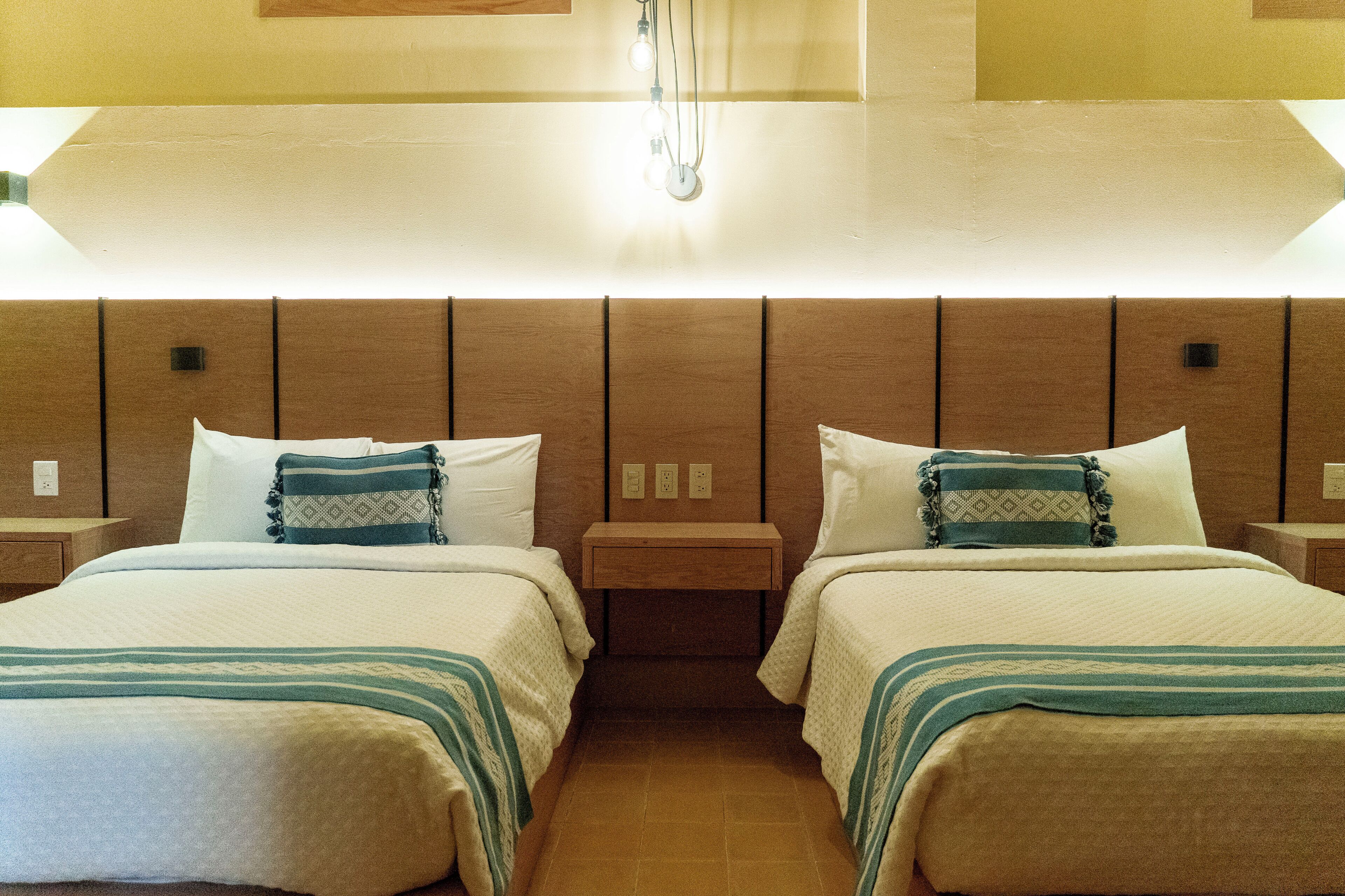 A hotel room with two beds, a wooden headboard, bedside tables, and a light fixture above the beds.