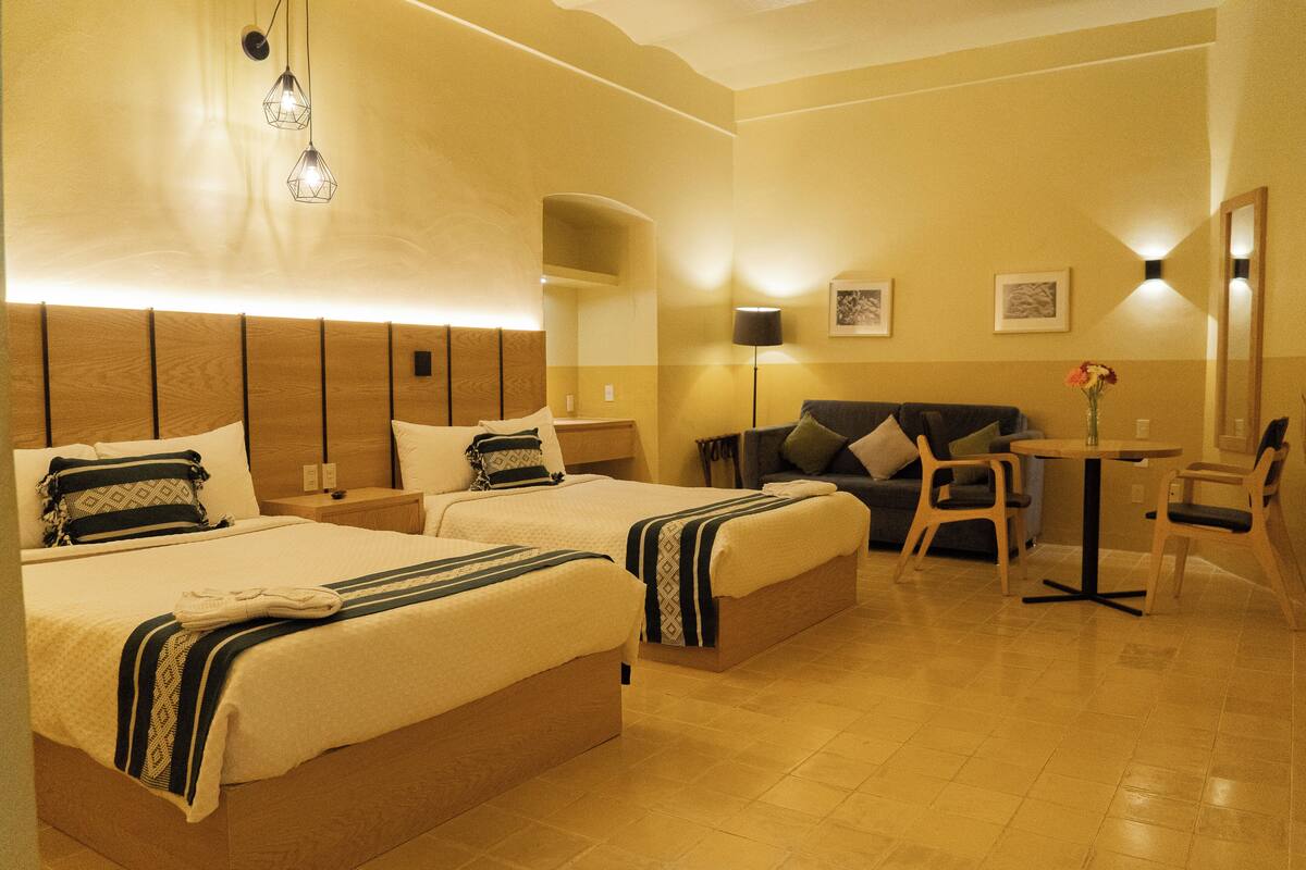A hotel room with two beds, a sofa, a small table, and a lamp.
