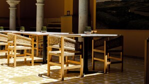 A dining area with wooden tables and chairs, columns, and a painting of a landscape.