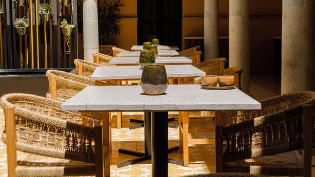 A row of tables with wicker chairs, a decorative vase, and a potted plant on each table.