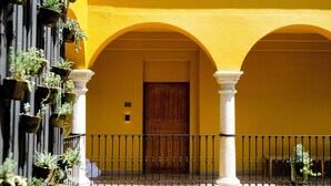 A yellow building with a wooden door, white columns, and a balcony with potted plants.