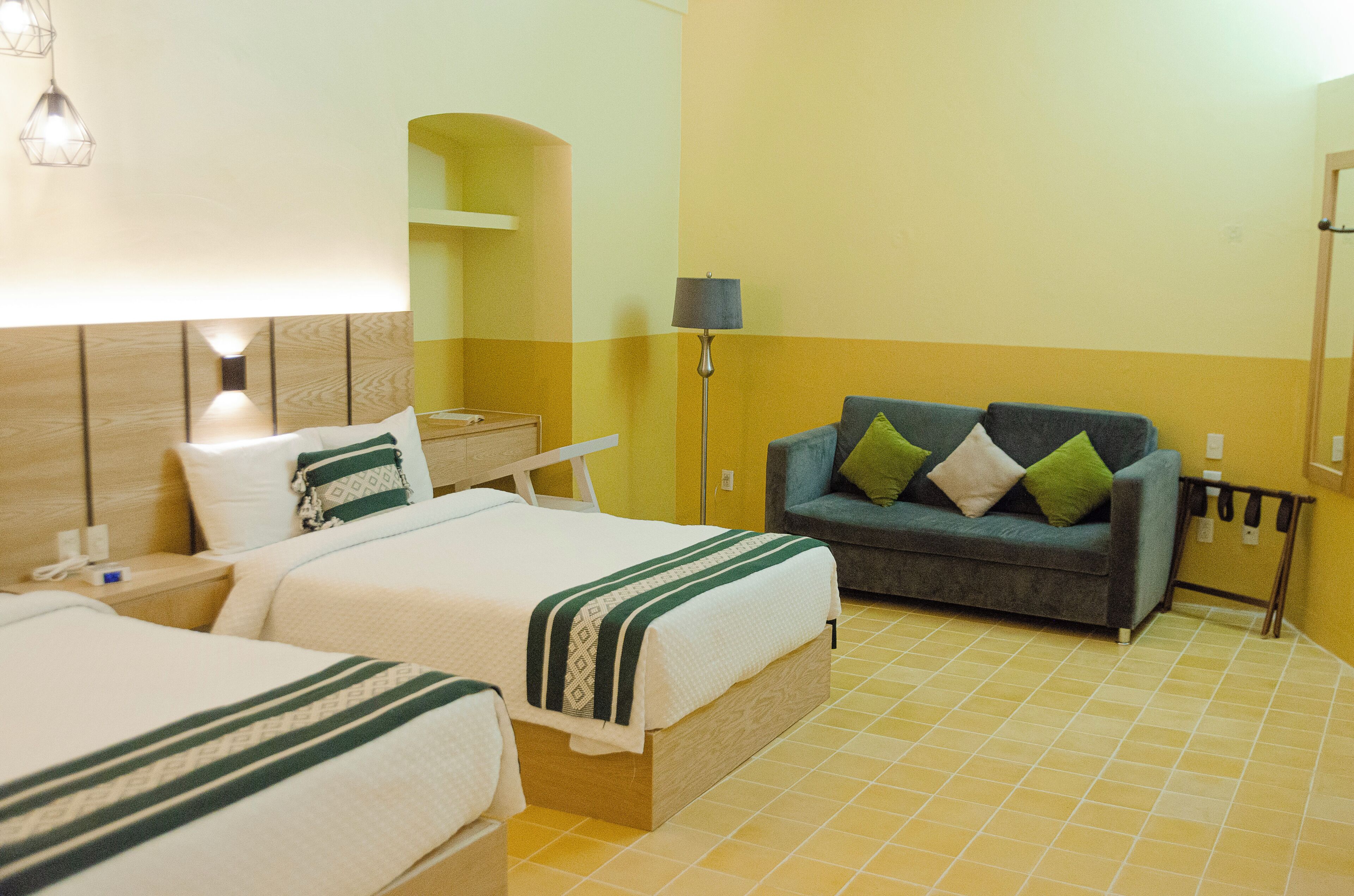 Camera d'albergo con due letti, un divano e una lampada.