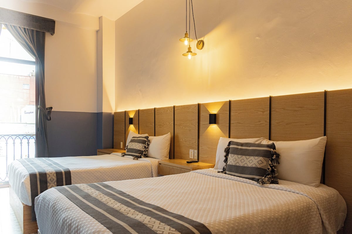 A hotel room with two beds, wooden headboards, and bedside lamps.