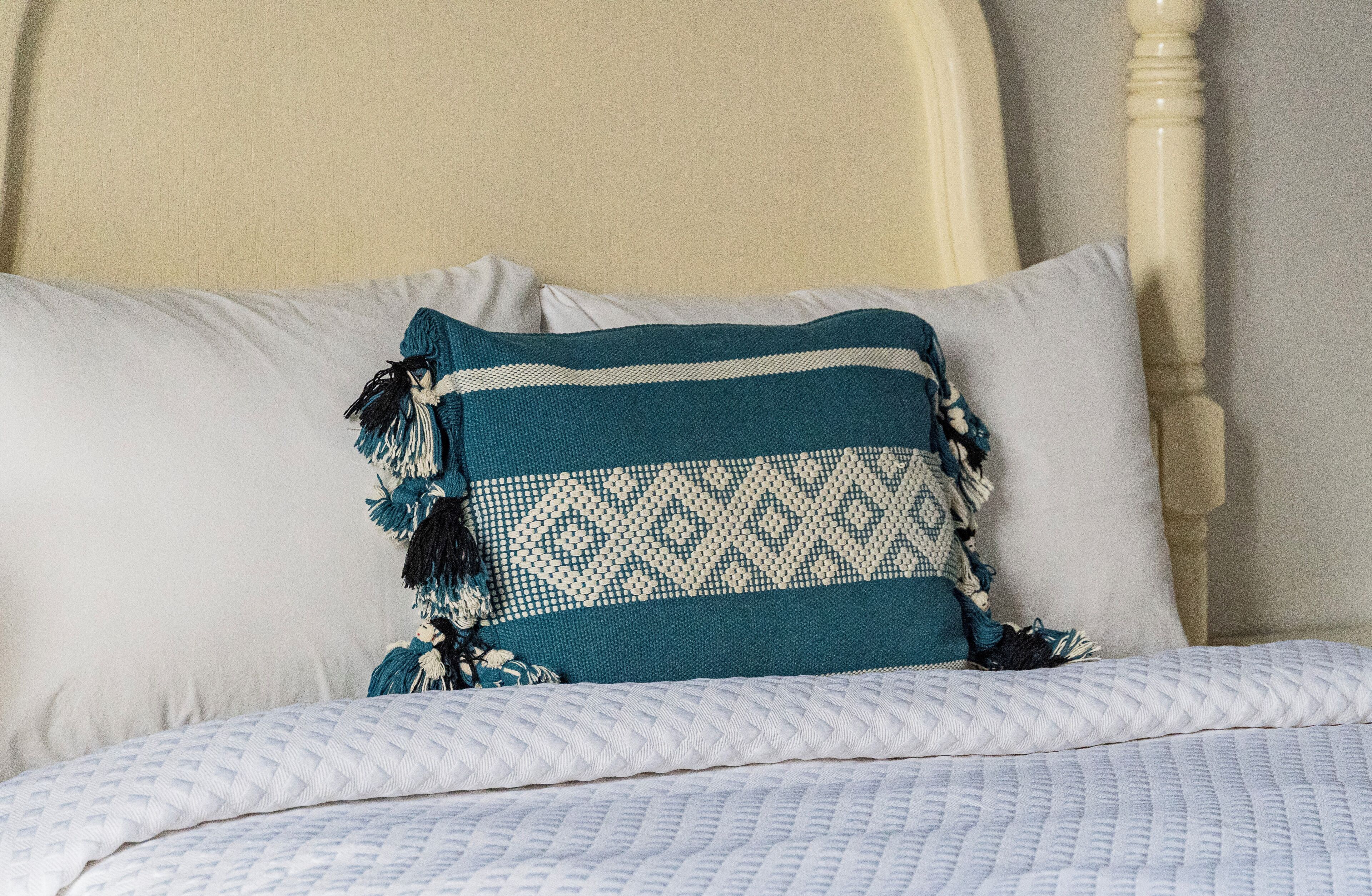 Una cama con cabecera blanca, almohada de diseño azul y blanco, y colcha blanca.