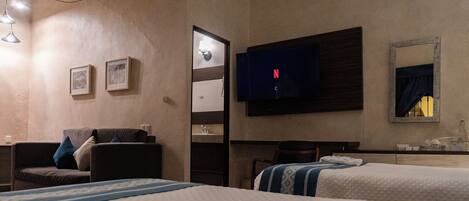 A hotel room with two beds, a TV, a desk, and a mirror.