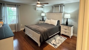 Une chambre à coucher avec un lit, deux tables de chevet, un ventilateur de plafond et une fenêtre avec des rideaux.