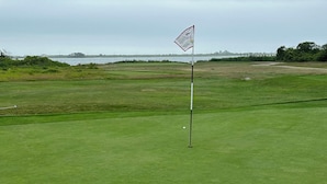 Un terrain de golf avec un mât de drapeau au premier plan et une étendue d’eau en arrière-plan.