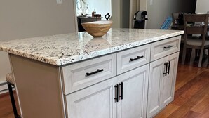 Une cuisine dotée d’un plan de travail en granit, de meubles blancs et d’un parquet en bois.