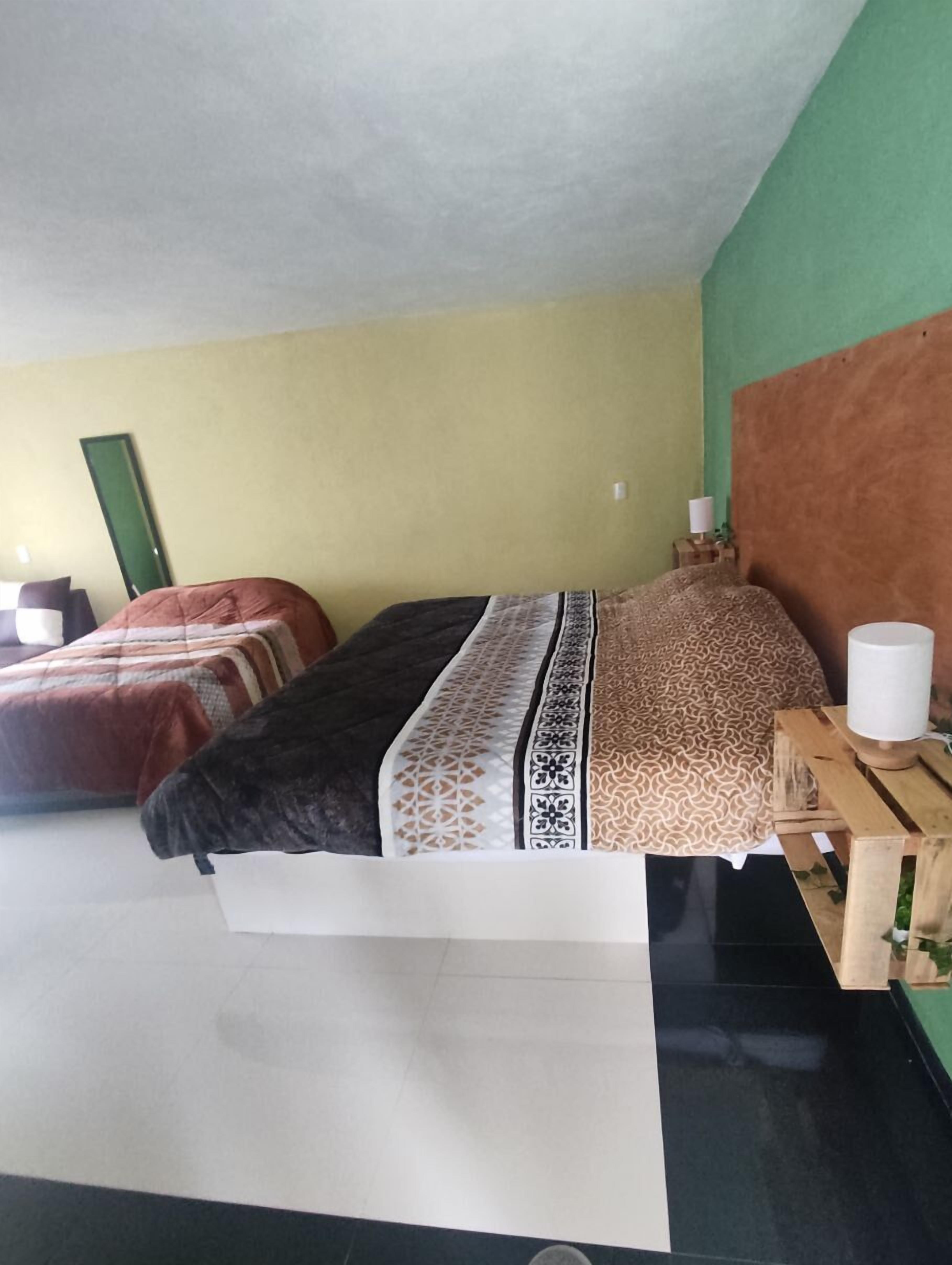 A bedroom with two beds, a green wall, a brown headboard, and a wooden nightstand with a lamp.
