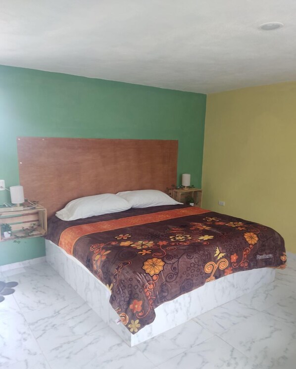 Een bed met een bloemenprint sprei, een houten hoofdbord en twee nachtkastjes met lampen.