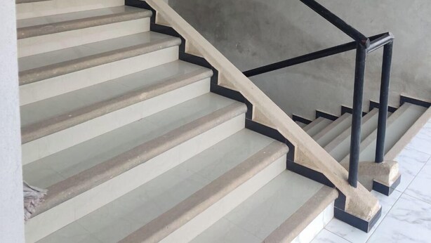 Een moderne trap met een betonnen muur en een zwarte metalen balustrade.