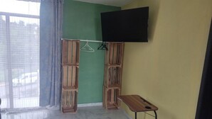 Een kamer met een groot raam, houten kasten, een aan de muur bevestigde televisie en een klein tafeltje.