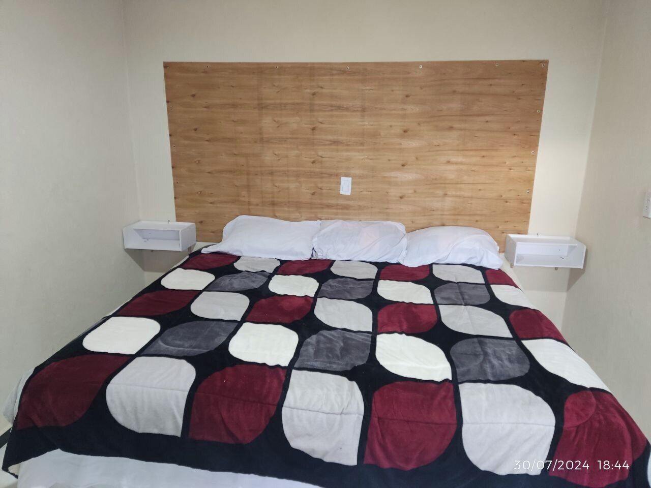 A single bed with a wooden headboard, white pillows, and a patterned bedspread.