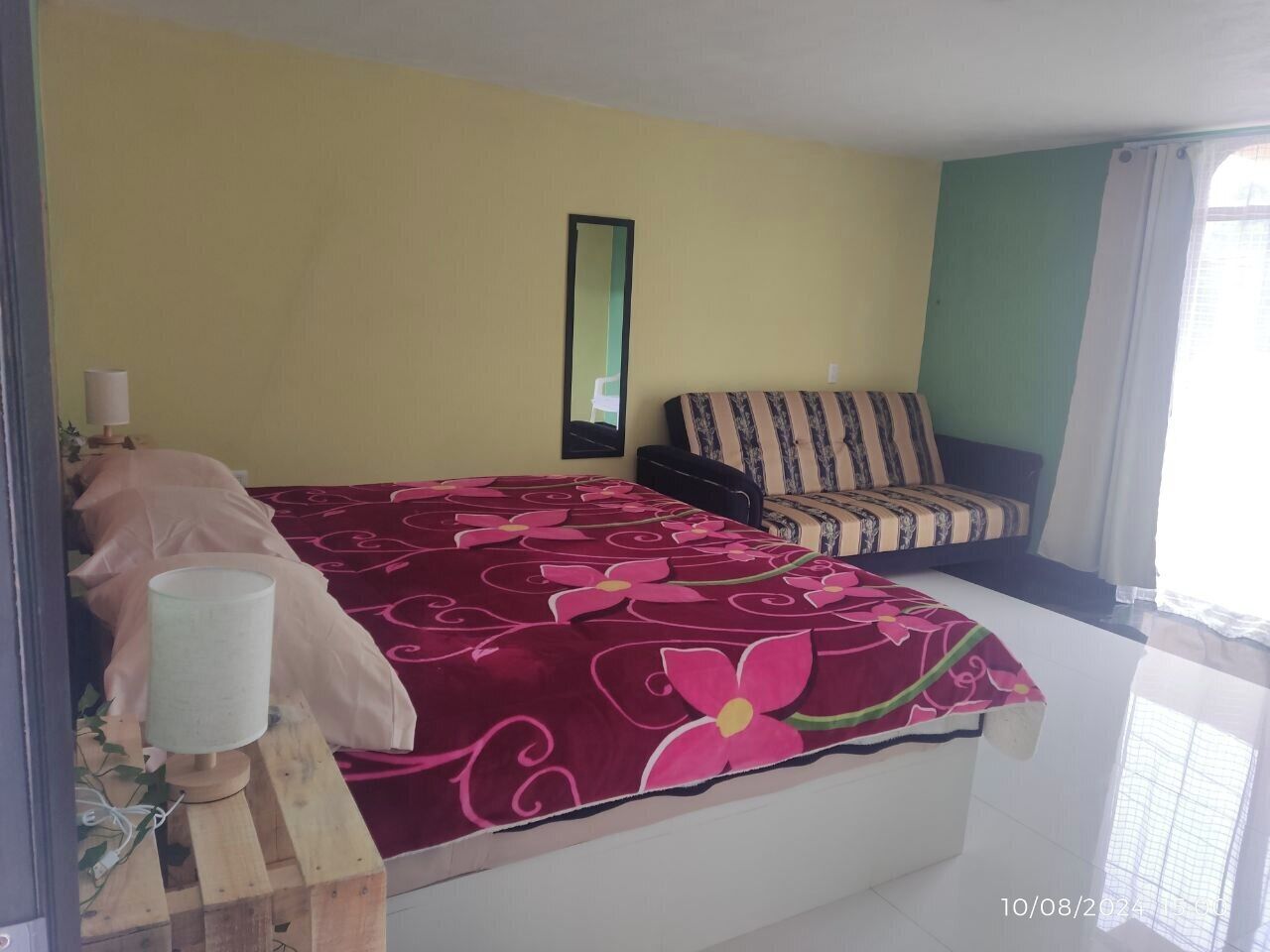 Un dormitorio con cama, mesita de noche, lámpara, silla y ventana con cortinas.