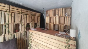 Een kamer met een wand van houten latten, een bureau met een lamp en planken met potplanten.