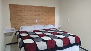 Een slaapkamer met een houten hoofdbord, een bed met een quilt met een patroon, witte kussens en een nachtkastje.