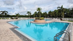 A large outdoor swimming pool with a circular center, surrounded by palm trees and lounge chairs.