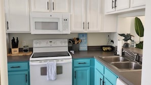 A kitchen with white cabinets, a white stove, a microwave, and a dishwasher. There is a teal-colored countertop and a rug on the floor.