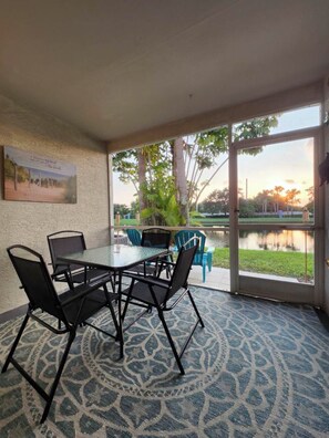 Habitación con mesa y sillas de vidrio, alfombra estampada y vista a un lago a través de amplias ventanas.