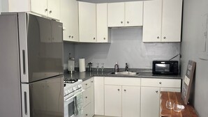 Eine kleine Küche mit weißen Schränken, einem Edelstahl-Kühlschrank, einer Mikrowelle und einem Gasherd.