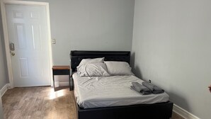 Ein Schlafzimmer mit schwarzem Bettgestell, weißer Bettwäsche, einem Holznachttisch und einer Tür mit Lichtschalter.