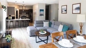 A modern living room with a grey sectional sofa, a wooden coffee table, and a dining area with a wooden table set for four. - Beautiful 3 Bedroom House w/ Hot Tub, Sauna & Private Yard - 2 Minutes to RMR (Revelstoke)