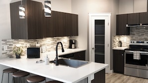 A modern kitchen with dark wood cabinets, a white countertop, a built-in oven, and a coffee maker. - Beautiful 3 Bedroom House w/ Hot Tub, Sauna & Private Yard - 2 Minutes to RMR (Revelstoke)