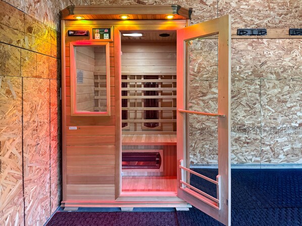 Una sauna con interior de madera, un panel de control y vistas al exterior a través de una puerta de cristal.