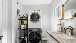 A compact laundry room with a front-loading washer and dryer, a countertop with a sink and soap dispenser, and a mirror above the sink. - Cozy 2bdr/1br Home near downtown (Sacramento)