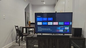 A modern living room with a flat-screen TV displaying a home screen with various streaming services. - Cozy 2bdr/1br Home near downtown (Sacramento)