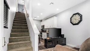 A staircase leading to a living area with a flat-screen TV, a clock, and a sofa. - Cozy 2bdr/1br Home near downtown (Sacramento)