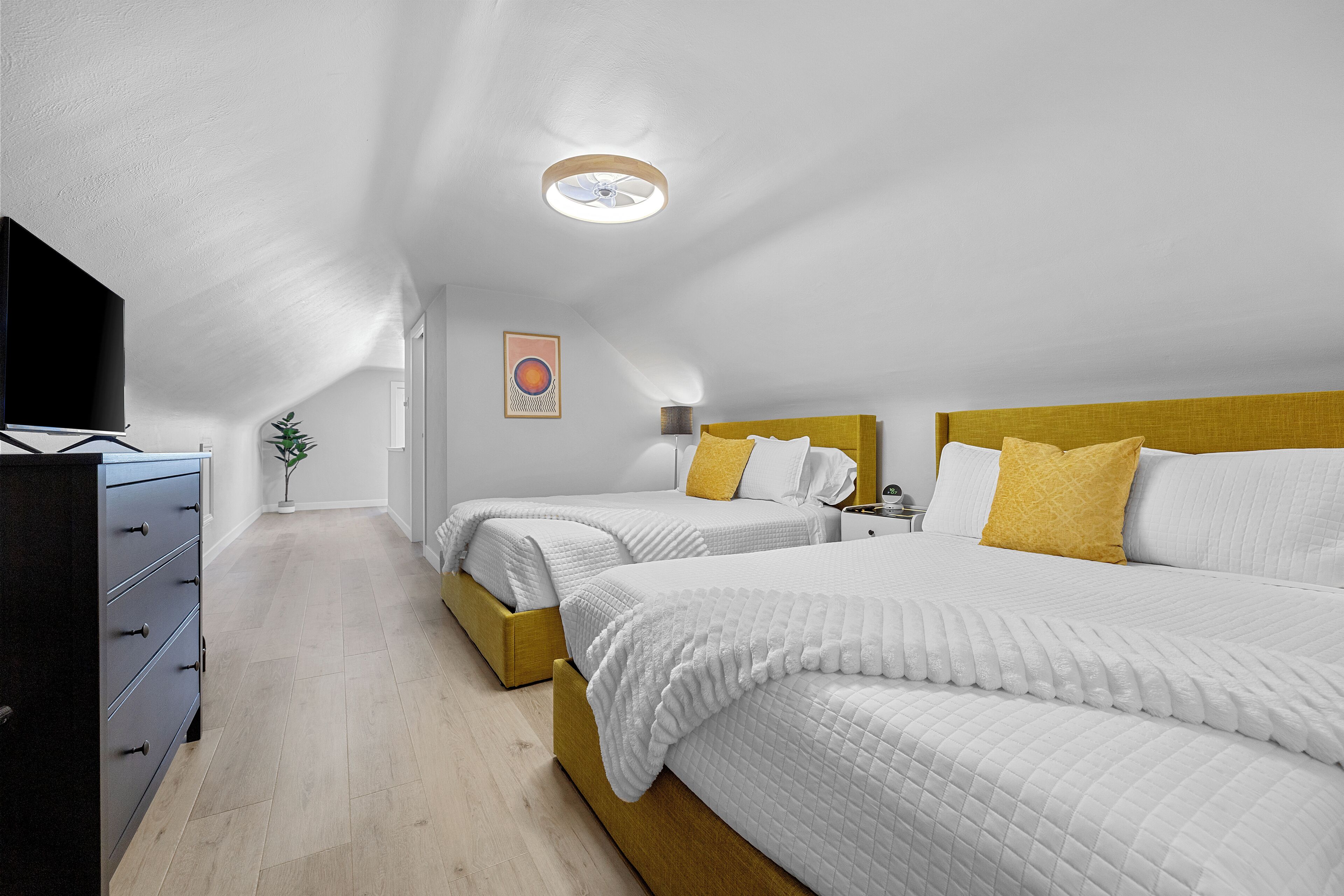 A bedroom with two beds, a dresser, a ceiling fan, and a wall-mounted TV.