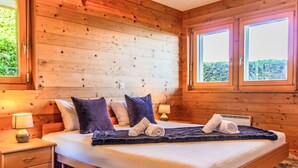 A wooden cabin-style bedroom with a bed, two nightstands, and a large window. - Chalet Aurore by Interhome (Nendaz)