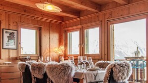 A wooden cabin interior with a dining table set for six, surrounded by chairs with fur trim. - Chalet Aurore by Interhome (Nendaz)