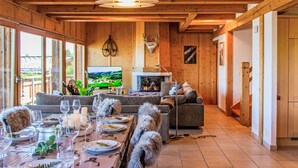 A cozy wooden interior with a dining area set for a meal, a fireplace, and a television displaying a scenic view. - Chalet Aurore by Interhome (Nendaz)