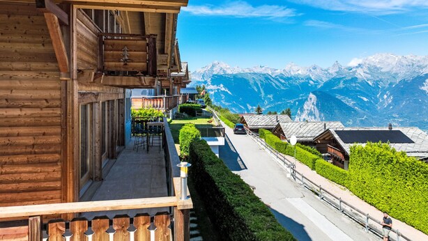 A wooden chalet with a balcony overlooking a mountain path and snow-capped peaks. - Chalet Aurore by Interhome (Nendaz)