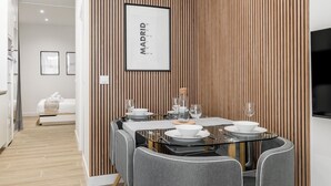 Uma sala de jantar moderna com parede de painel de madeira, um mapa emoldurado de Madri e uma mesa de vidro preparada para quatro pessoas.