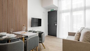 Quarto de hotel moderno com área de refeições, televisão de tela plana, sofá e uma grande janela.
