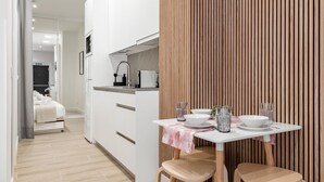 A modern kitchen with white cabinets, a wooden accent wall, and a dining area with a table set for two.