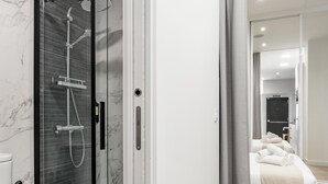 A modern bathroom with a glass shower enclosure, a toilet, and a bed with neatly folded towels.
