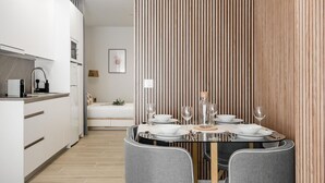 A modern kitchen with white cabinets, a dining area with a round table and grey chairs, and a wooden slatted partition. - Charming Madrid Castilla II - Studio for 4 people (Madrid)