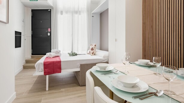Une chambre d’hôtel moderne, équipée d’un lit, d’une petite table à manger pour deux personnes et d’un escalier menant à une sortie.