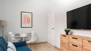 A modern living room with a blue sofa, a dining table with chairs, a flat-screen TV, and a minimalist cabinet. - Villa de Vallecas I - One-bedroom apartment (Madrid)