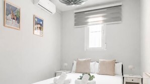 A neatly arranged bedroom with a bed, bedside tables, and a window with blinds. - Villa de Vallecas I - One-bedroom apartment (Madrid)