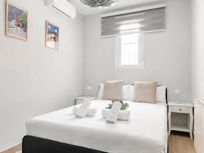 A neatly arranged hotel room with a bed, bedside tables, a window with blinds, and wall-mounted air conditioning. - Villa de Vallecas I - One-bedroom apartment (Madrid)