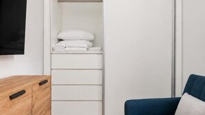A room with a wooden dresser, a blue sofa, and a white closet with a television mounted on the wall. - Villa de Vallecas I - One-bedroom apartment (Madrid)