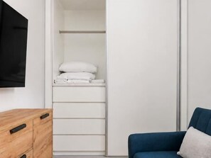 A room with a wooden dresser, a blue sofa, and a white closet with a television mounted on the wall. - Villa de Vallecas I - One-bedroom apartment (Madrid)