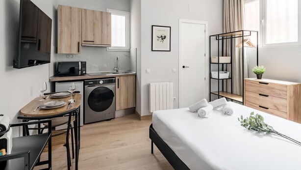 Un appartement moderne et compact comprenant une kitchenette, un coin repas et une chambre.