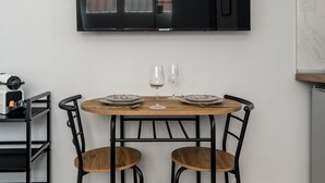 Un coin repas comprenant une table ronde en bois, deux chaises et un téléviseur à écran plat fixé au mur.