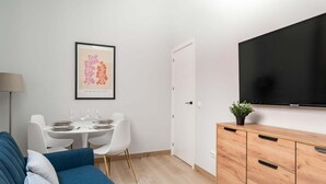 Una sala de estar moderna con sofá, mesa de comedor, sillas, televisor y aparador.